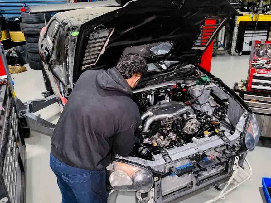 Garage Full Throttle mechanic conducting a detailed under-bonnet inspection on a stripped performance car, checking engine and mechanical components as part of a comprehensive vehicle assessment in Melbourne.