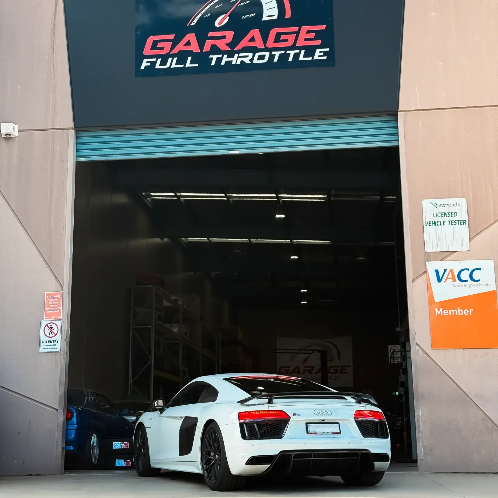 White Audi R8 entering Garage Full Throttle's Craigieburn workshop, with VicRoads Licensed Vehicle Tester and VACC member accreditation visible at the entrance.