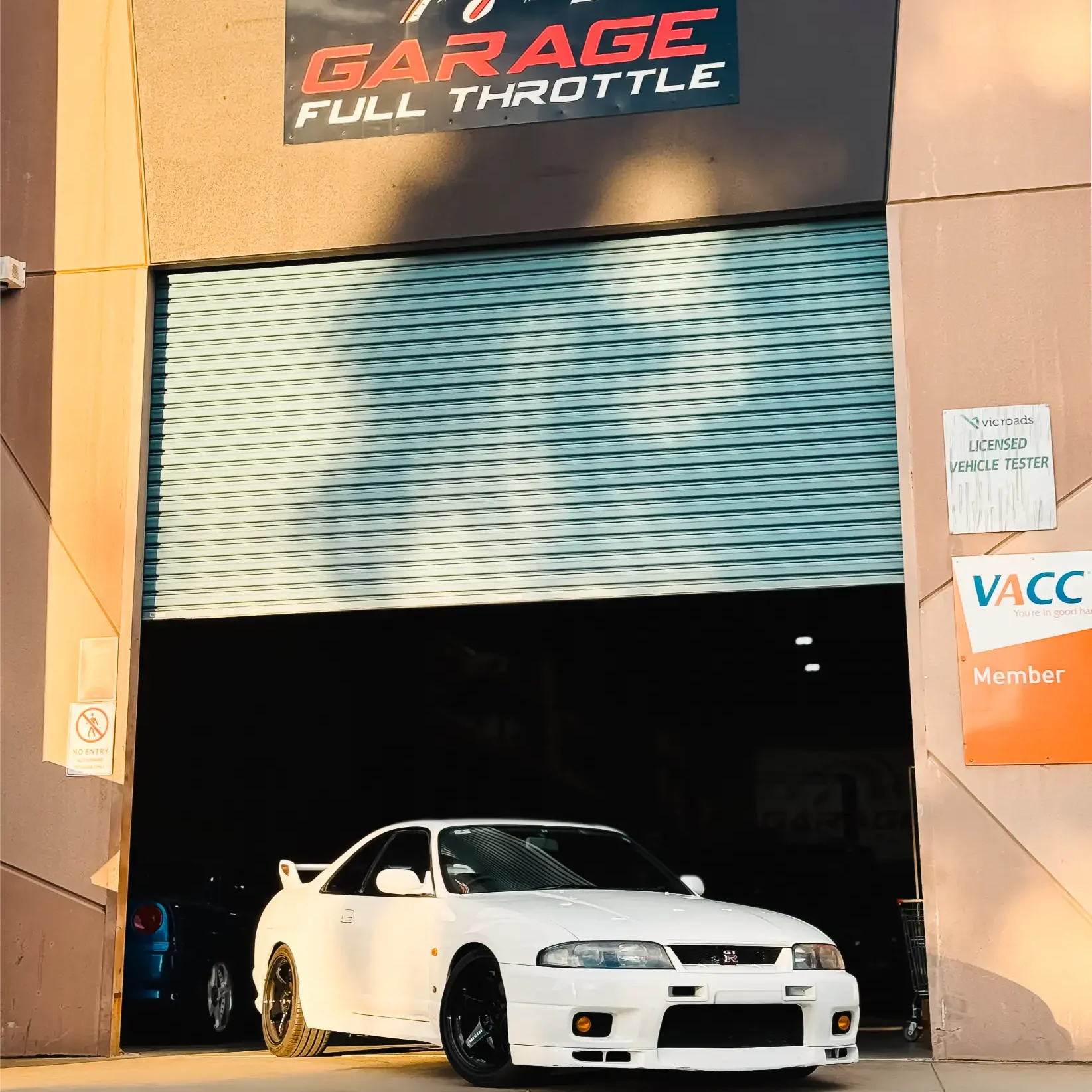 White Nissan Skyline GT-R parked outside Garage Full Throttle's Craigieburn workshop, with VicRoads Licensed Vehicle Tester and VACC member accreditation visible at the entrance.