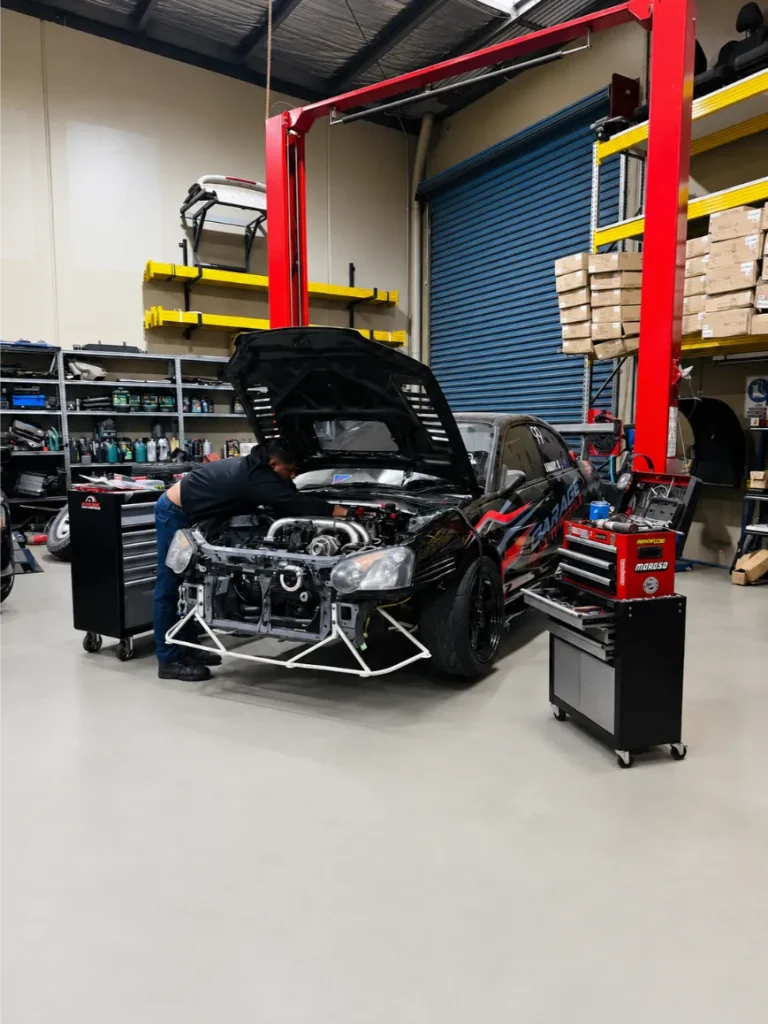 Garage Full Throttle mechanic inspecting the engine bay of a modified black performance car with front panels removed, inside a professional automotive workshop in Melbourne's northern suburbs.