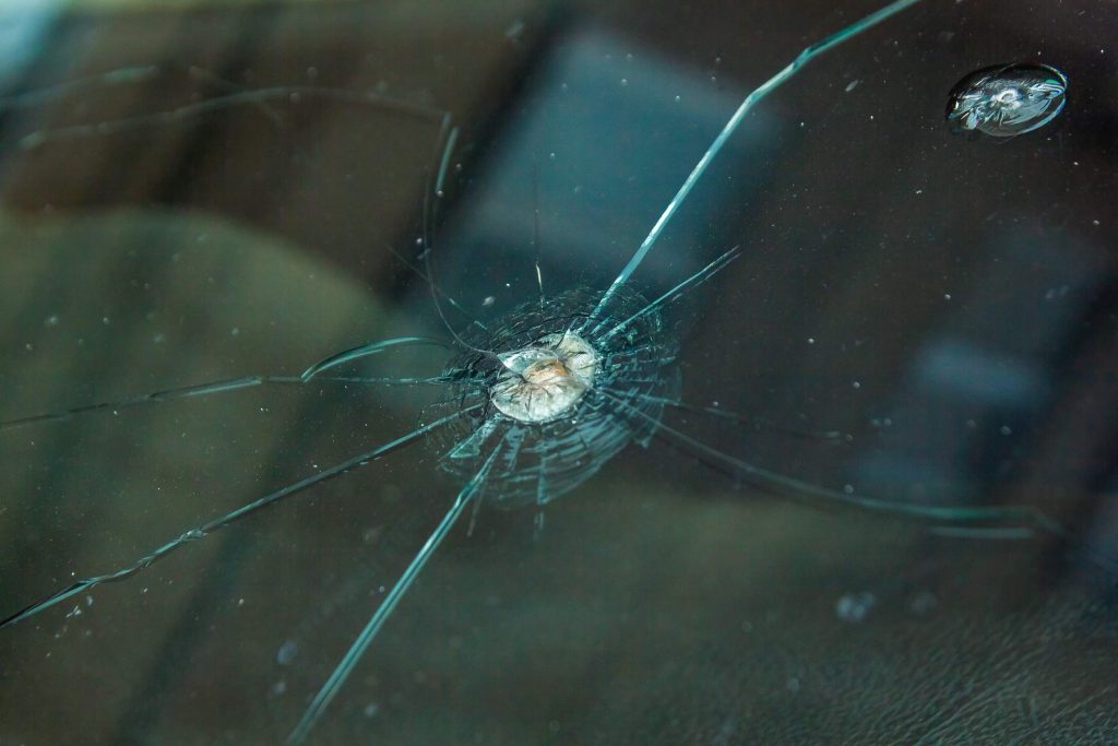 Close-up of a cracked car windscreen with a stone chip impact point and multiple spreading cracks radiating outward, the type of damage that causes a roadworthy certificate failure in Victoria.