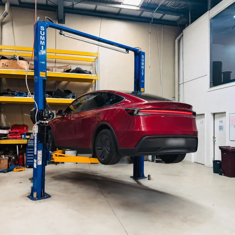 Red electric Tesla Model Y raised on a hoist during an EV Roadworthy Certificate inspection at Garage Full Throttle Craigieburn
