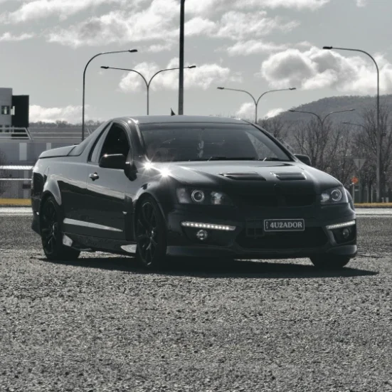 Black modified Holden ute parked outdoors with custom headlights and body kit.